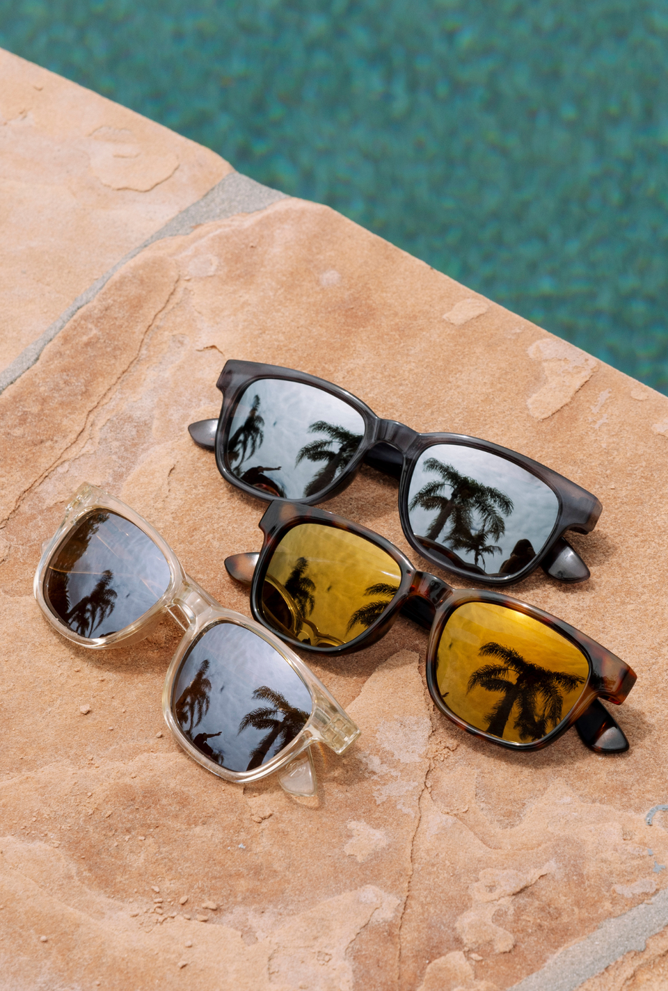 Three pairs of sunglasses sitting by a pool