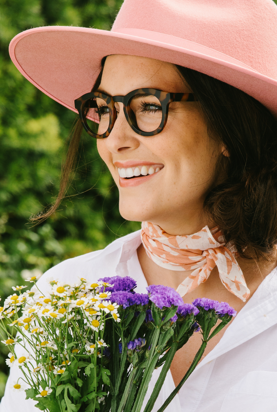 Model wearing brown reading glasses outside holding flowers