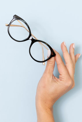 a hold holding up black Marquee reading glasses with a light blue background